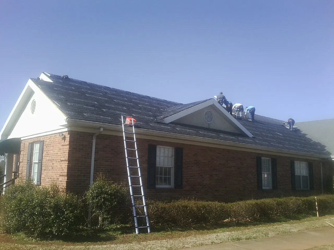 Crew tearing shingles off a brick ranch roof with a ladder set — Metal Roof Repair work by our crew in Riverside