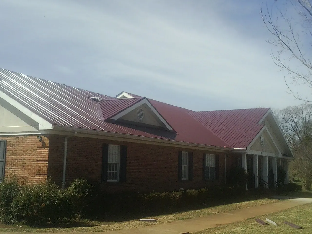 Red metal roof with gabled entries on a long brick building, from a Hail Damage Roof Repair job in Riverside
